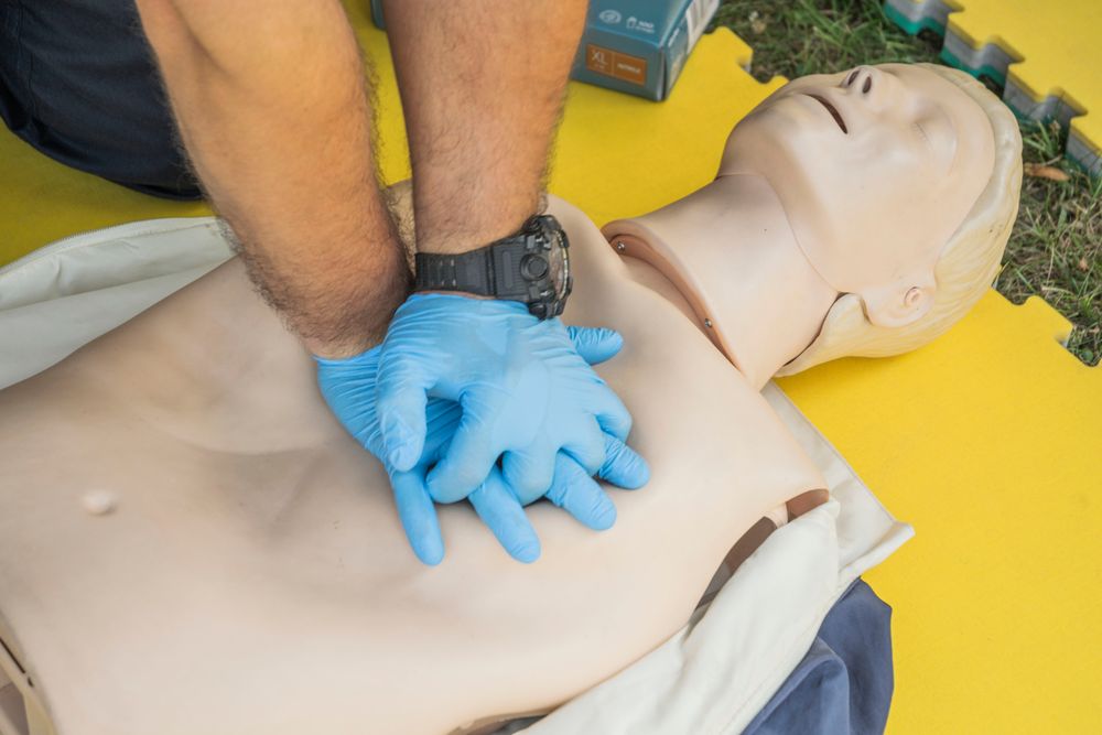 Stock photograph of gloved hands practicing chest compressions on a CPR manikin